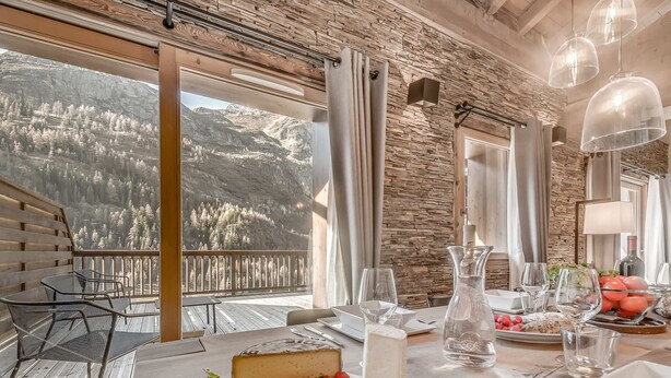 Ein Essbereich mit Tisch für zwei Personen, Käseplatte und Blick auf eine Berglandschaft.