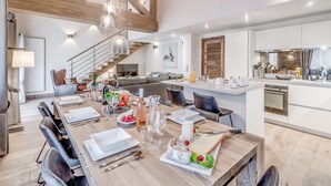 Eine moderne Küche mit einer zentralen Kochinsel, ein Essbereich mit einem Holztisch, der für eine Mahlzeit gedeckt ist, und eine Treppe, die in einen oberen Bereich führt.