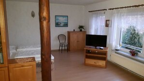 Una sala de estar con un mueble bajo de madera para el televisor, un sofá, una silla y un ventanal con cortinas.
