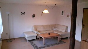 Un salón con un sofá color beige, una mesa de centro de madera, una alfombra estampada, una lámpara de pie y adornos de mariposas en la pared.