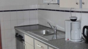 Una cocina con microondas, lavamanos, cafetera y armarios.