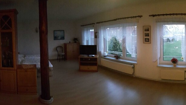 Una sala de estar con un mueble de madera, un televisor, una ventana que ofrece vistas a un paisaje verde y un radiador.
