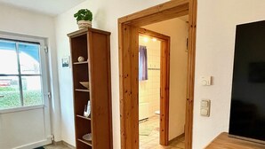 Una habitación con una estantería de madera, una puerta que da al baño y un televisor sobre un mueble de madera.