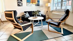 Una sala moderna con un sofá, dos sillones, una mesa de centro y una lámpara colgante.