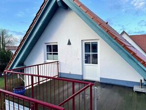 A house with a steeply pitched roof, a white exterior, and a red railing in the foreground.