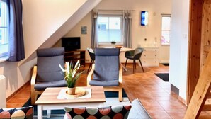 Un espacio de sala de estar acogedor con un sofá, dos sillones, una mesita con una planta y un televisor.