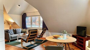 Un espacio habitable estilo loft acogedor con techo alto, un sofá, sillas, una mesa de comedor y un televisor.