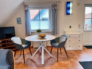 Un salon chaleureux avec une table ronde, deux chaises, un téléviseur et une fenêtre avec des rideaux.