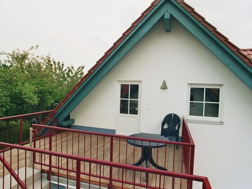 A two-story house with a red railing, a balcony, and a table with chairs.