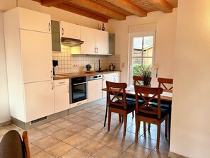 Une cuisine moderne avec des meubles blancs, un plan de travail en bois et un coin repas comprenant des chaises et une table en bois.