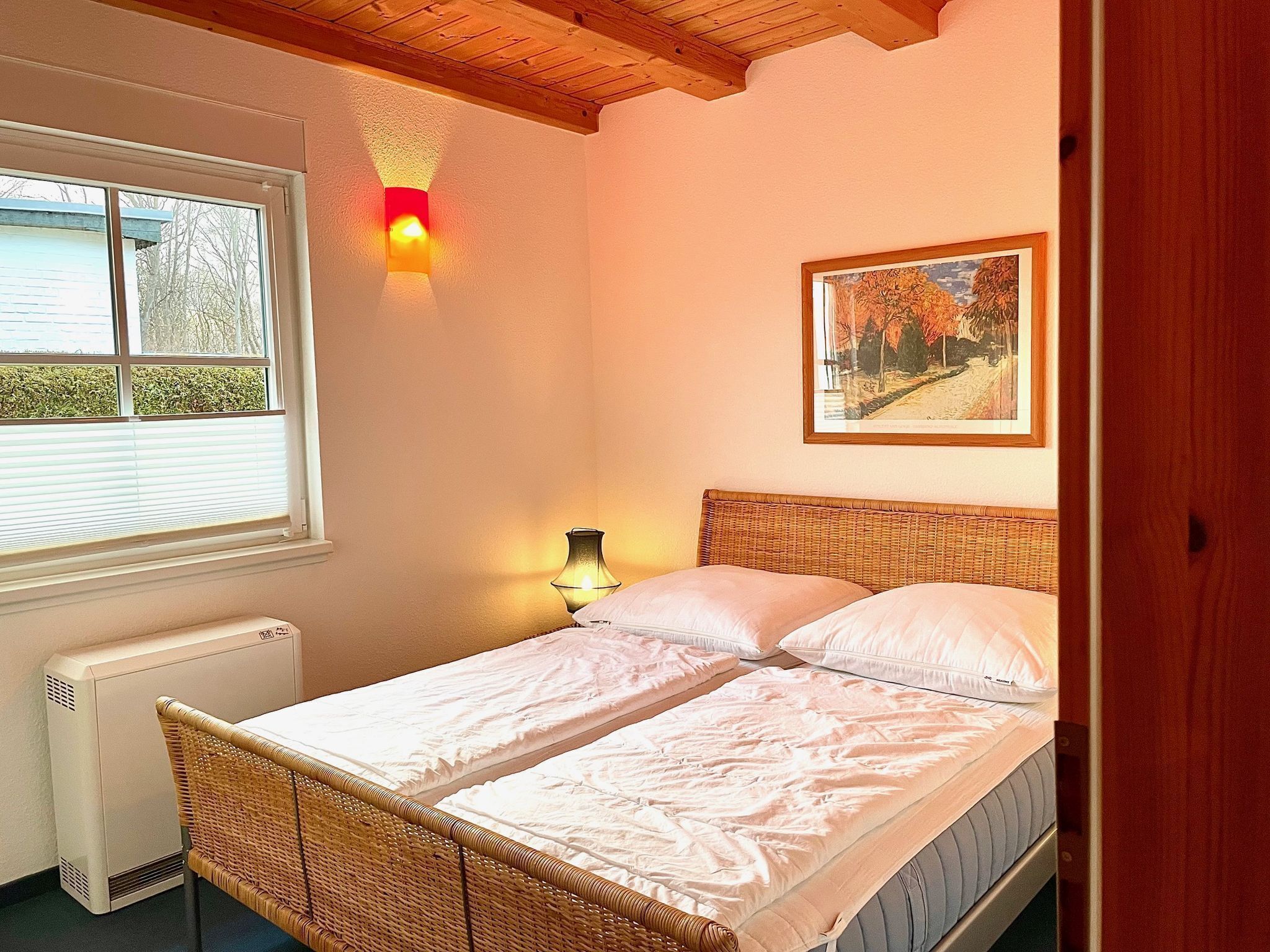 Ein Schlafzimmer mit einem Bett, einem Fenster, einem Heizkörper, einer Wandlampe und einem gerahmten Bild.