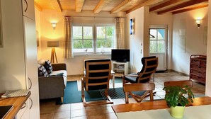 A cozy living room with a wooden ceiling, a television, two chairs, a sofa, and a dining table.