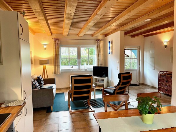 A cozy living room with a wooden ceiling, a television, two chairs, a sofa, and a dining table.
