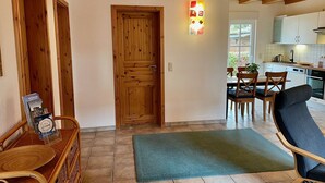 A cozy interior with a wooden door, a dining area with chairs, and a kitchen in the background.