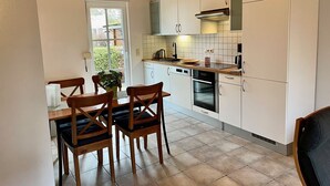 A compact kitchen with white cabinets, a wooden dining table with chairs, a window, and a built-in oven.