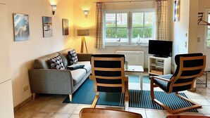 A living room with a sofa, two chairs, a television, and a window with curtains.