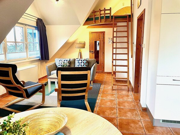 Une pièce chaleureuse avec un lit en mezzanine, un coin repas avec une table et des chaises, et un espace cuisine.