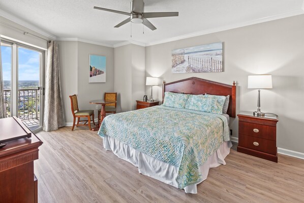 A bedroom with a large bed, a desk, a chair, a nightstand, and a ceiling fan.