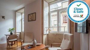 Una sala de estar moderna con piso de madera, una mesa de centro redonda, dos sillones blancos, una mesita con una planta y un cuadro en la pared.