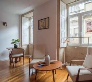Un salon moderne avec un plancher en bois, une table basse ronde, deux fauteuils blancs, une petite table avec une plante et un tableau encadré au mur.