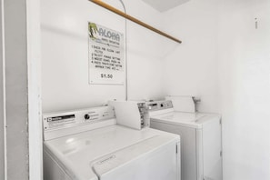 A laundry area with two white washing machines, a sign detailing the dryer's operation, and a price tag of $1.50.