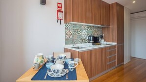 A modern kitchen with wooden cabinets, a tiled backsplash, and a dining area set with blue and white tableware. - TORRINHA H - Charming studio located in the artistic district of Miguel Bombarda (Porto)