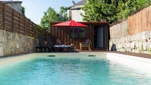 Una piscina con poltronne da relax e un ombrellone rosso.