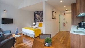 Una moderna camera d'albergo con un letto, una scrivania, una sedia, una televisione e un angolo cottura.