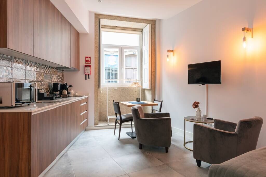 A modern kitchen with wooden cabinets, a dining area with a table and chairs, and a TV mounted on the wall.