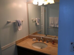 Une salle de bain avec un lavabo, deux robinets, un miroir et un porte-serviettes avec des serviettes.