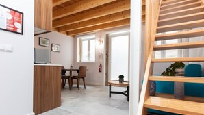 Un interior moderno con una escalera de madera, un comedor con mesa y sillas, y una cocina con refrigerador y lavaplatos.