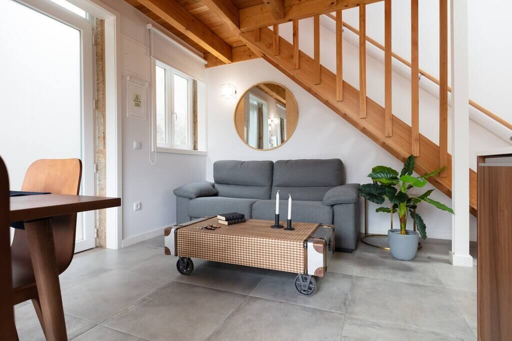 Een moderne woonkamer met een grijze bank, een houten salontafel en een trap met houten leuningen.