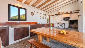 A kitchen with a wooden table, a bench, and a fireplace. - Beautiful Vacation Home "Can Faveta" with Mountain View, Pool, Wi-Fi (Alcudia)