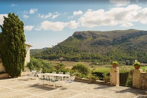 A patio with a table and chairs, a tall tree, and a view of a mountainous landscape. - Beautiful Vacation Home "Can Faveta" with Mountain View, Pool, Wi-Fi (Alcudia)