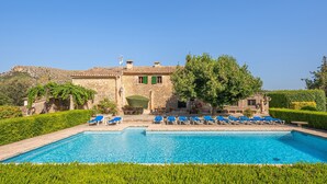 A pool with lounge chairs, a stone building with a green door, and a clear blue sky. - Beautiful Vacation Home "Can Faveta" with Mountain View, Pool, Wi-Fi (Alcudia)