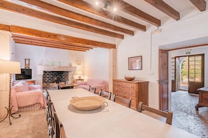Una habitación acogedora con chimenea, vigas de madera, una mesa de comedor y un sofá rosa.