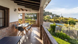 An outdoor patio with a table and chairs, a stone wall, and a view of a residential area. - Holiday Home “Villa Damian” with Mountain View and Garden (Málaga)