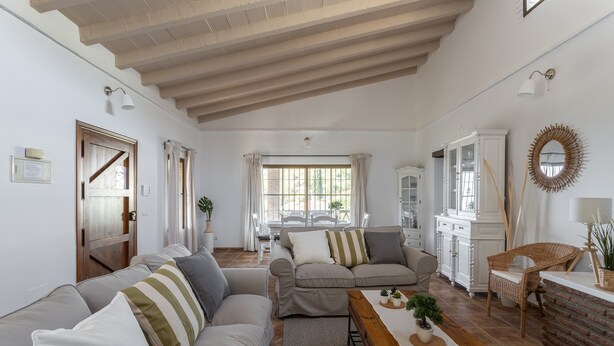 A spacious living area with a wooden ceiling, a dining table with a bench, and a kitchen area with white cabinetry. - Holiday Home “Villa Damian” with Mountain View and Garden (Málaga)