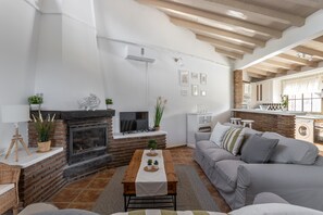 Una sala de estar con chimenea, sofá, mesa de centro y una zona de cocina con lavadora.