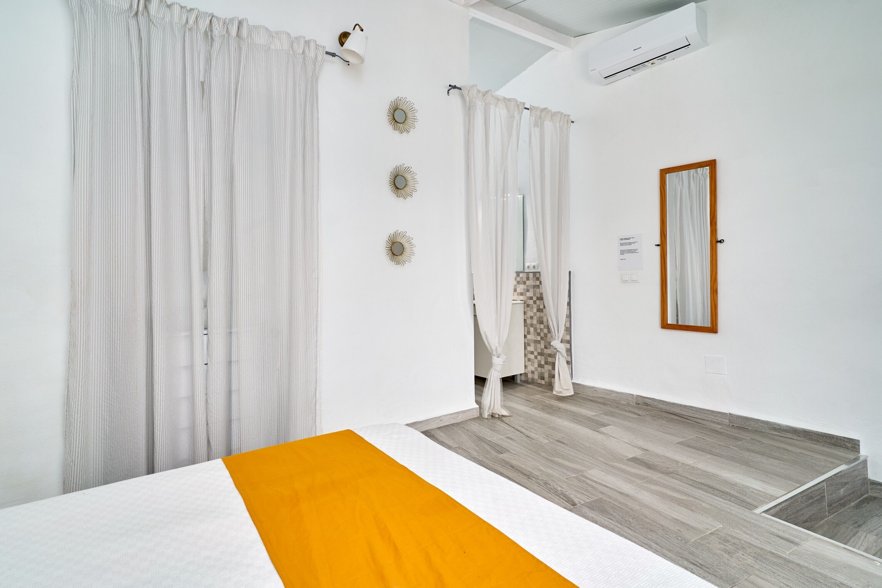 Ein Hotelzimmer mit Bett, Vorhängen, einem Spiegel und Holzboden.