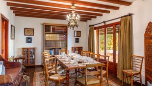 A dining room with a wooden table set for six, surrounded by chairs, a chandelier, and bookshelves filled with books. - Villa Bon Viure with Sea View, Wi-Fi, Air Conditioning, Pool, Garden & Terraces; Parking Available (Marratxí)