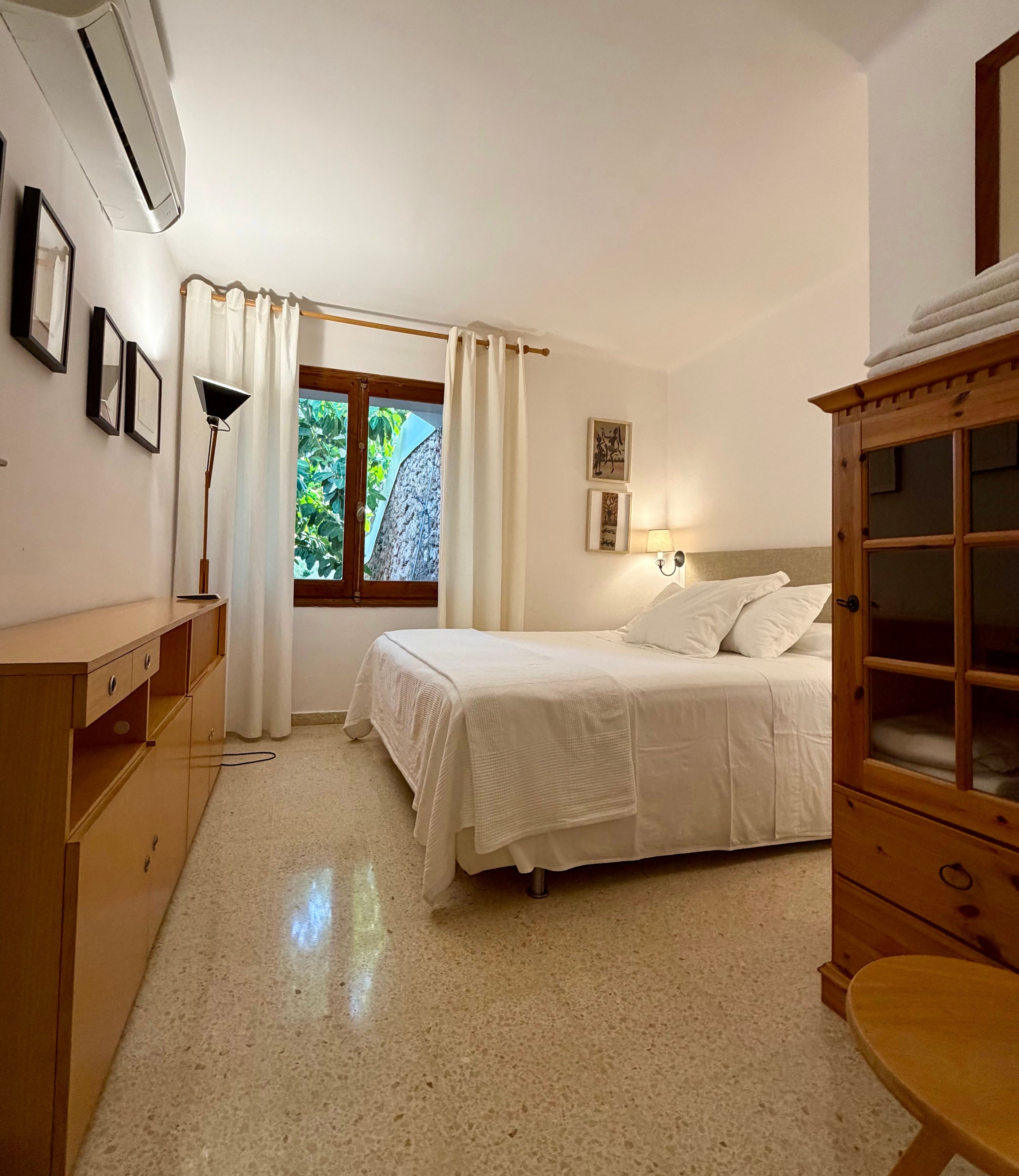 Un dormitorio con cama, escritorio, lámpara y ventana con cortinas.