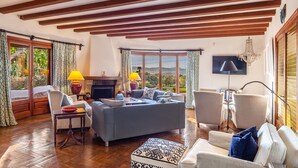 A spacious living room with a fireplace, comfortable seating, and large windows offering a view of the outdoors. - Villa Bon Viure with Sea View, Wi-Fi, Air Conditioning, Pool, Garden & Terraces; Parking Available (Marratxí)