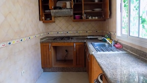 Een kleine keuken met houten keukenkastjes, een gasfornuis en een spoelbak.