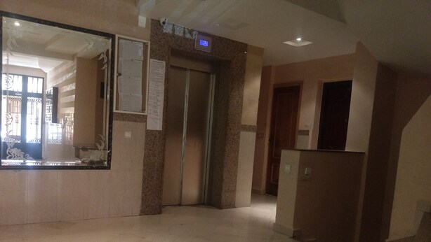 Een hotel lobby met een receptiebalie, een grote spiegel, een prikbord en een lift.