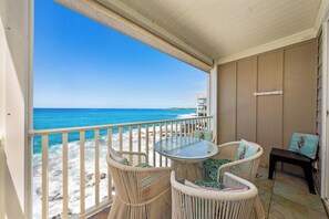 Een balkon met rieten meubels en een glazen tafel met uitzicht op een strand.