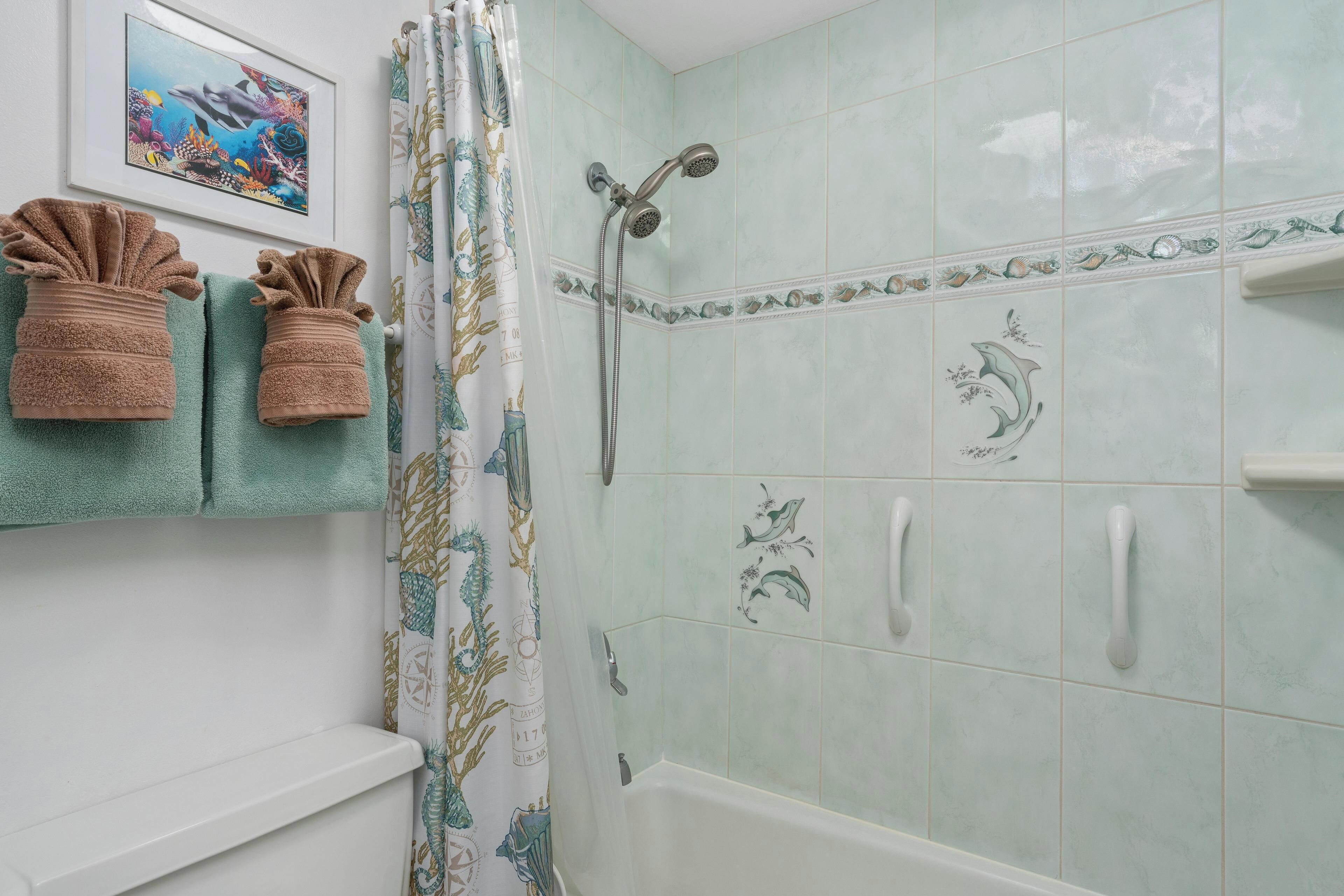 Une salle de bain avec une douche, un tableau encadré au mur et des serviettes suspendues à un porte-serviettes.