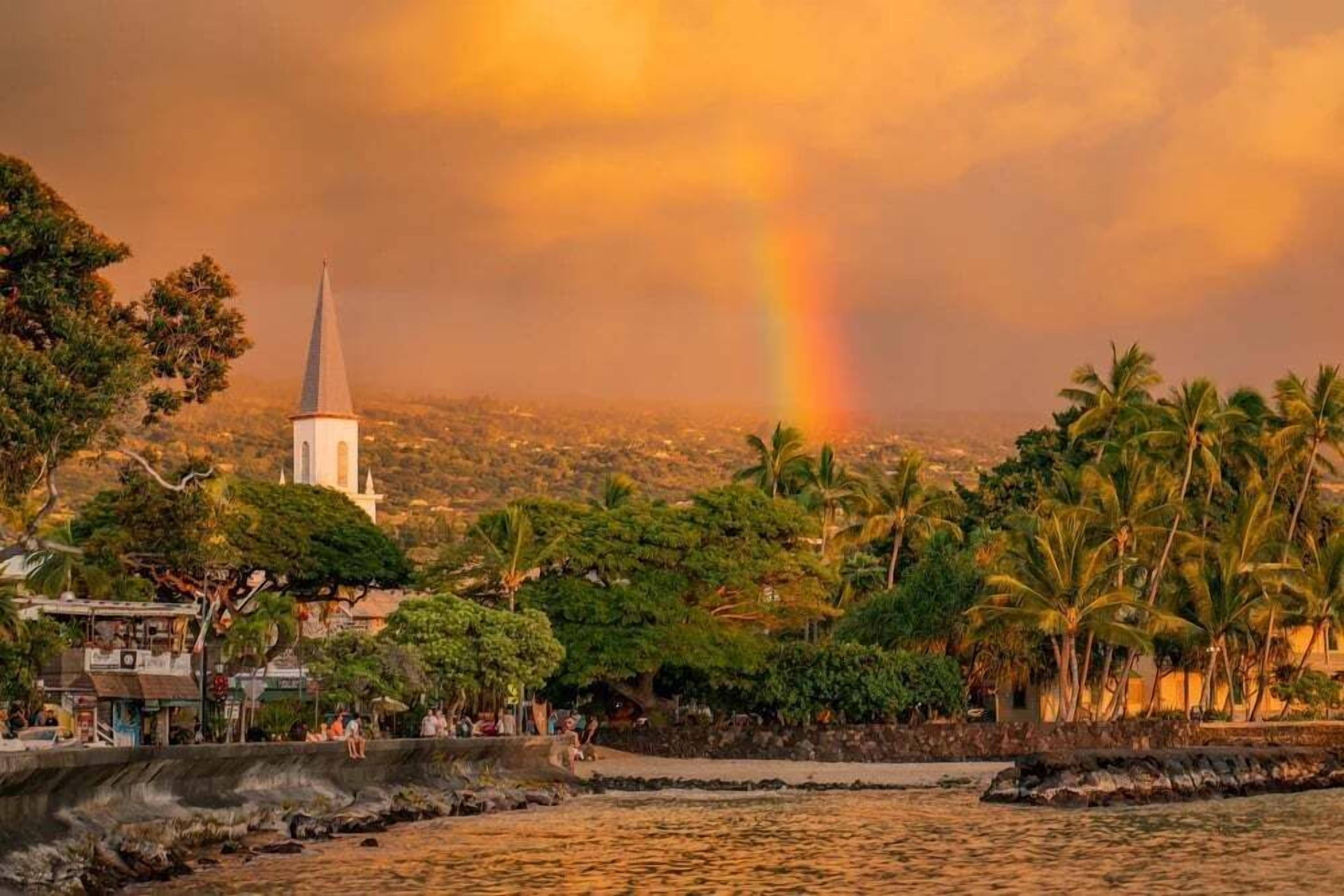 Vista costera con una aguja de iglesia, palmeras y un arcoíris.