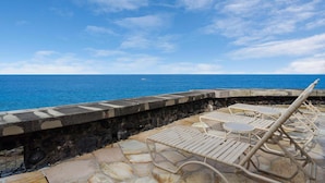 A seaside terrace with lounge chairs and a stone wall overlooking the ocean.