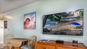 A room with a dining table, chairs, a TV on the wall, and a wooden dresser.